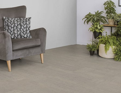 Der Boden im Wohnzimmer ist mit hellgrauem Kork belegt. Es gibt einen bequemen Sessel und einen Ständer mit Grünpflanzen.