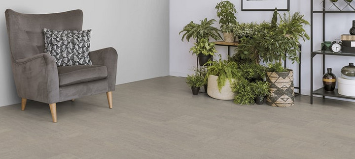 Der Boden im Wohnzimmer ist mit hellgrauem Kork belegt. Es gibt einen bequemen Sessel und einen Ständer mit Grünpflanzen.